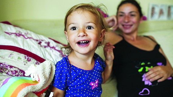 little girl smiling with mother watching behind her