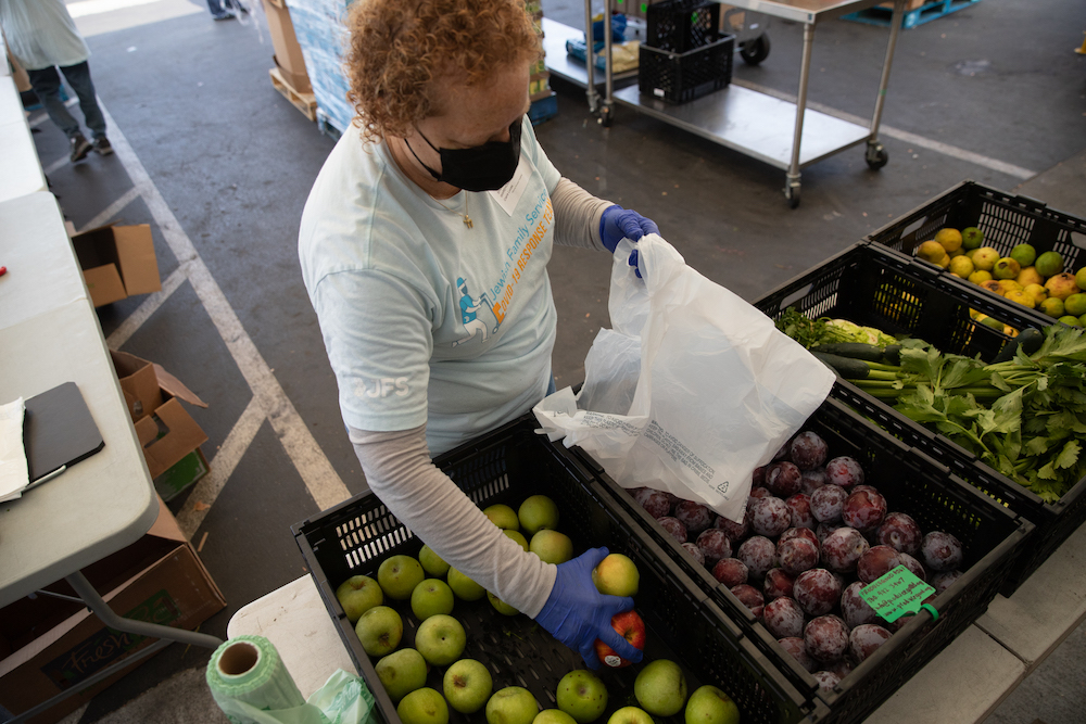 Volunteer picking fruit from a basket and placing into a plastic bag.